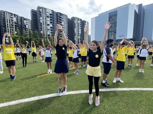 ​Stamford American students take time during Global Be Well Day to do stretching exercises on the sports field and dance to music.